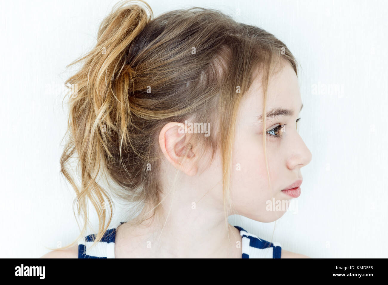 Cute girl eleven years old with blond long hair on white wall background in profile Stock Photo