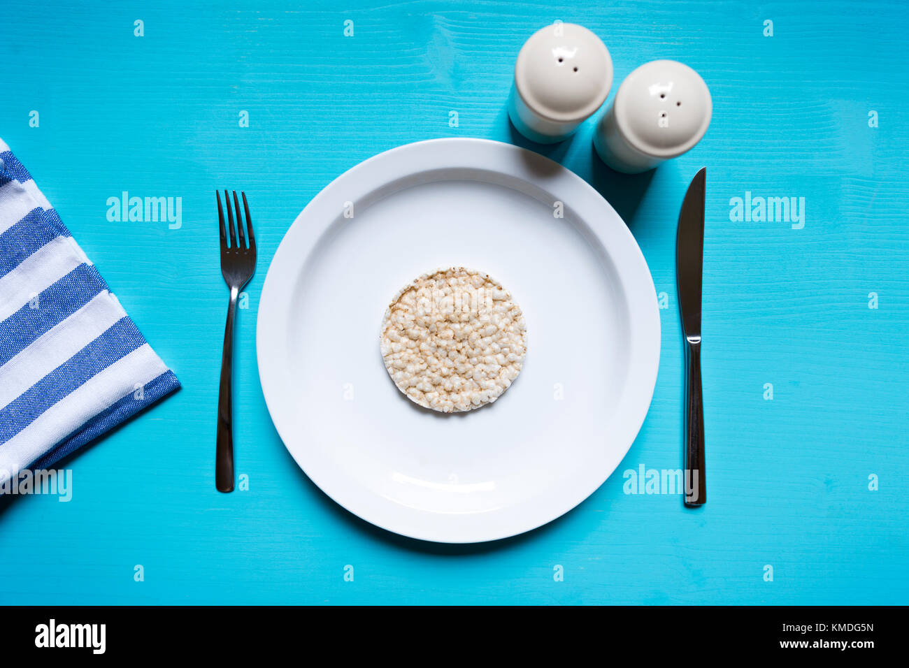 Diet concept. Rice pop cake on a white plate sitting on a blue turquoise wooden table. Table set for light breakfast Stock Photo