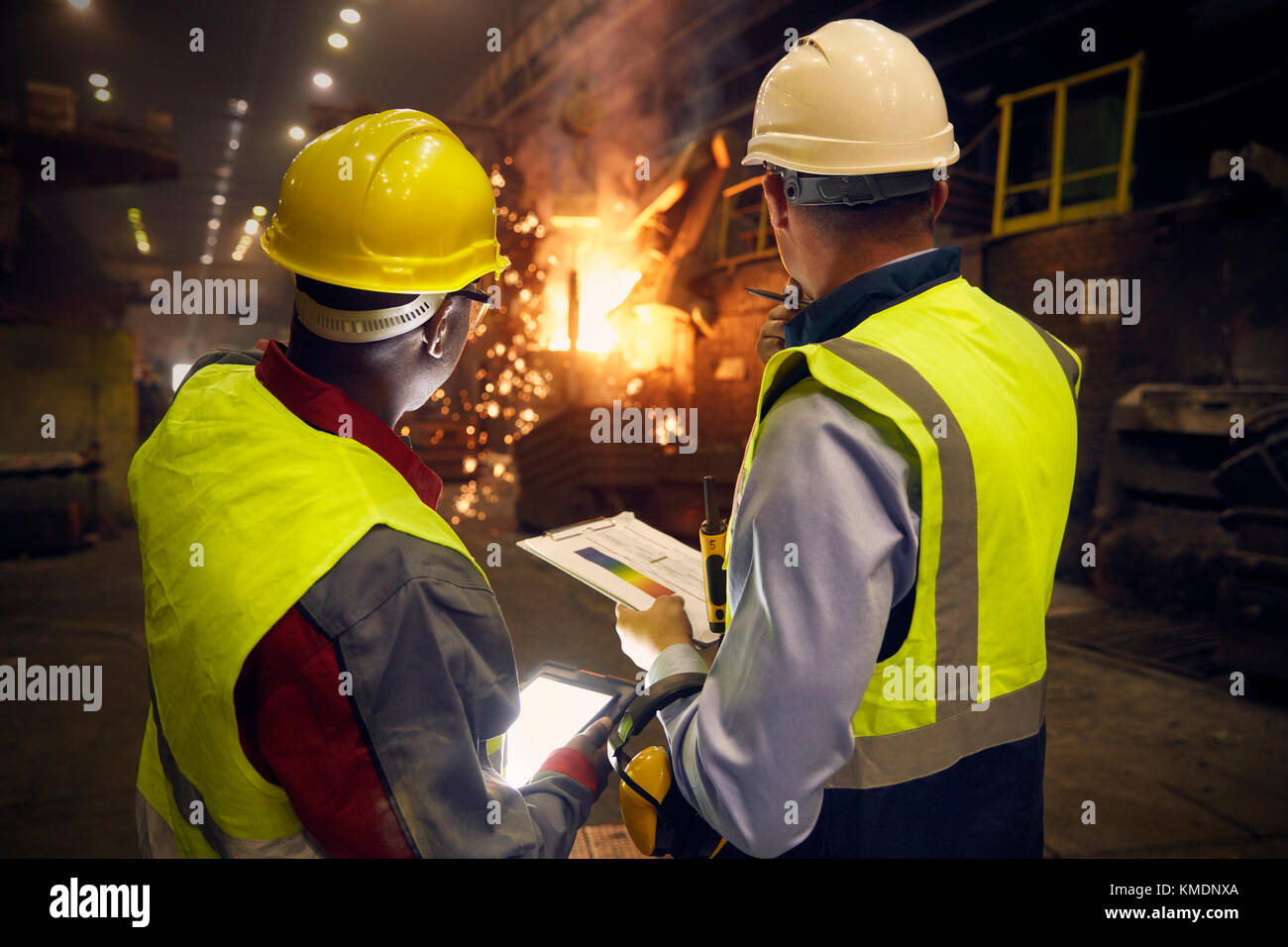 Steelworkers with digital tablet and clipboard talking in steel mill