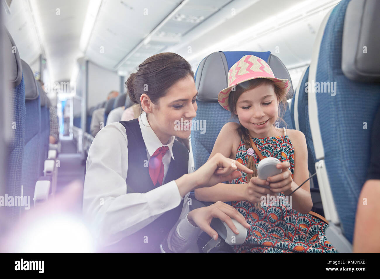 Flight attendant helping girl passenger with remote control on airplane Stock Photo