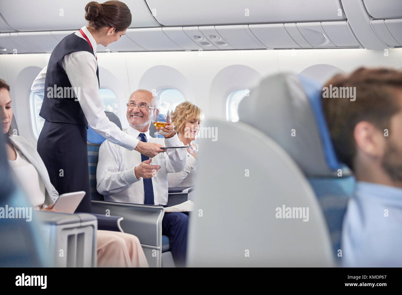 Flight attendant serving whiskey to businessman in first class on airplane Stock Photo