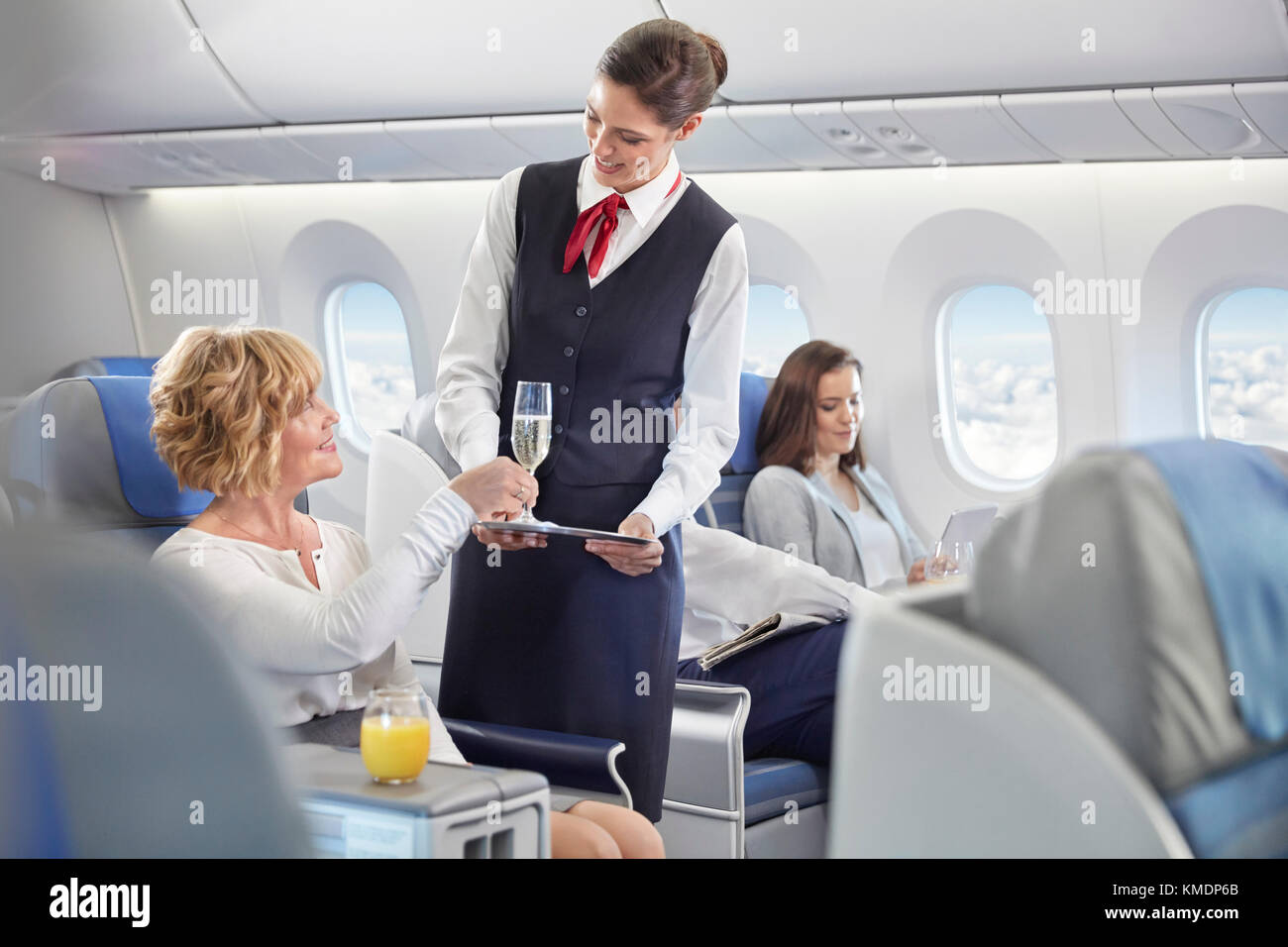 Flight attendant serving champagne to woman in first class on airplane Stock Photo