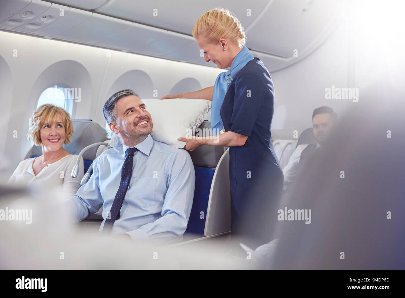 Smiling flight attendant adjusting pillow for businessman in first class on airplane Stock Photo