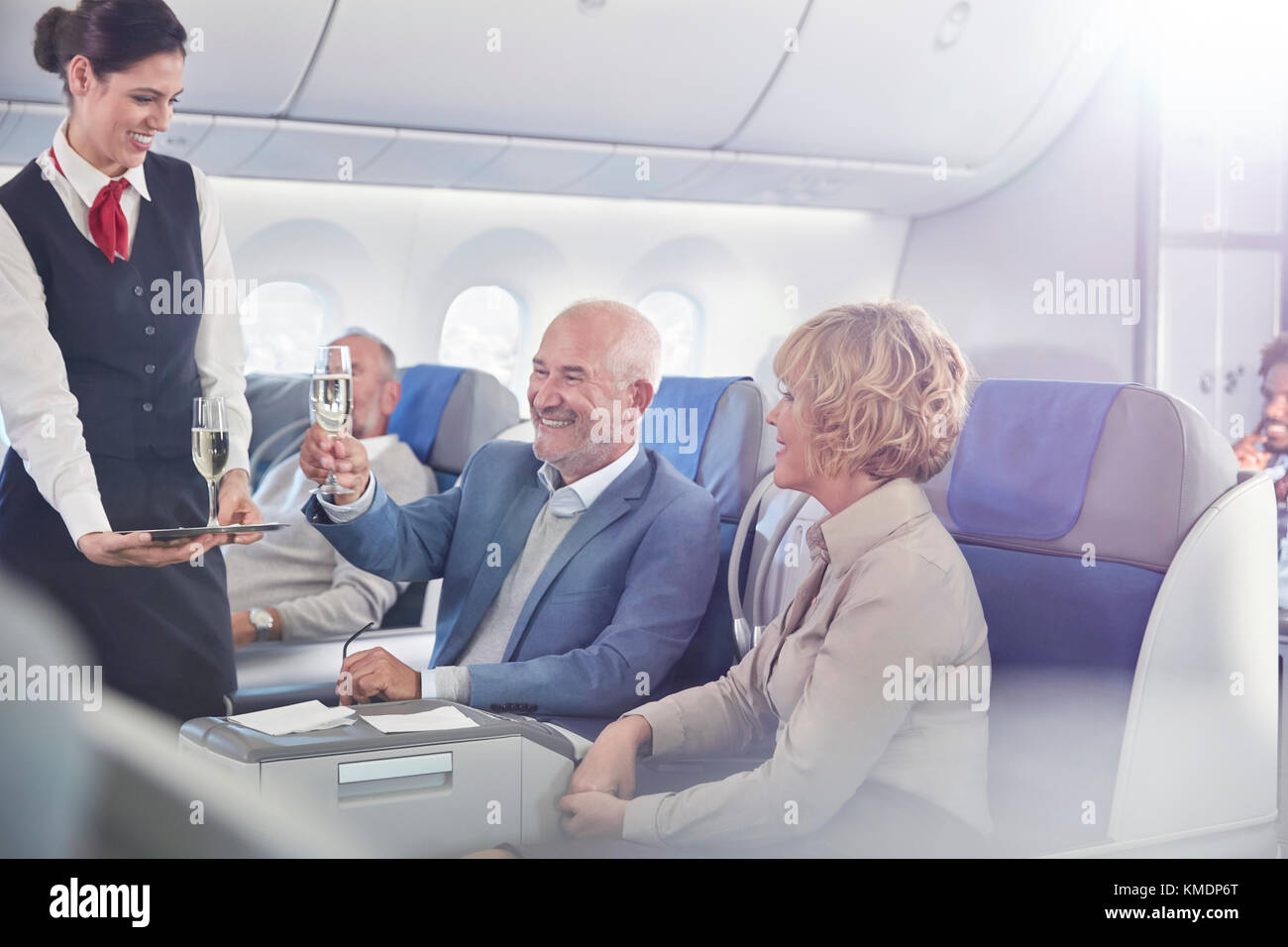 Flight attendant serving champagne to mature couple in first class on airplane Stock Photo