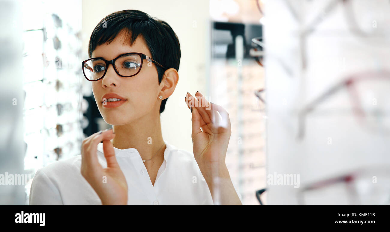 health care, eyesight and vision concept - happy woman choosing glasses at optics store Stock Photo