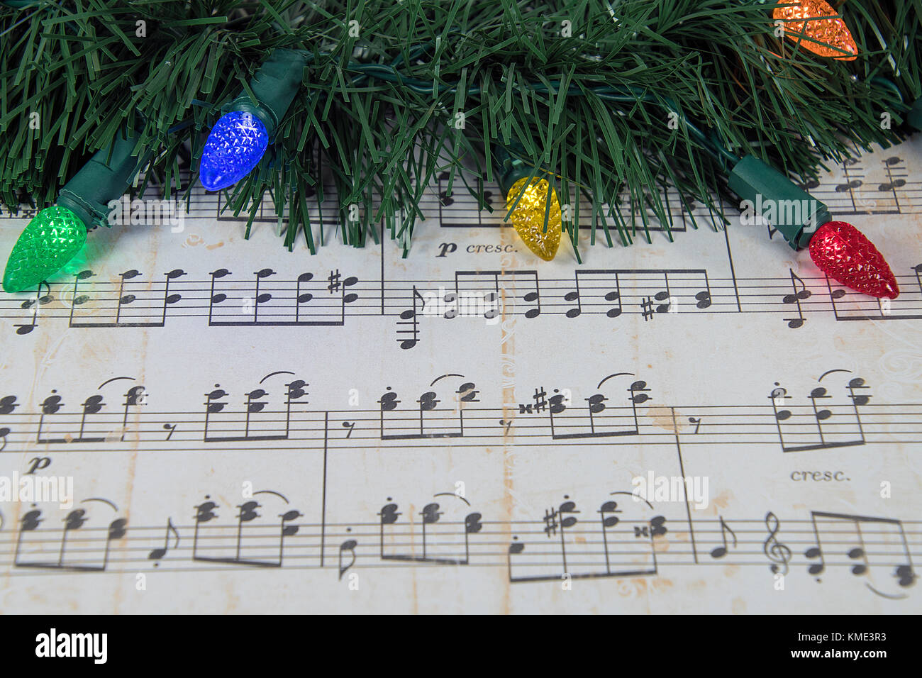 colorful holiday lights and green garland on worn sheet music Stock