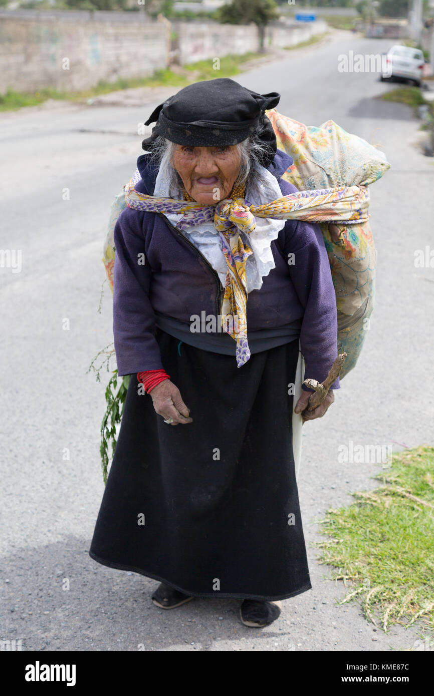 Mature indigenous woman in traditional costume carrying goods walking along a road, northern Ecuador, South America Stock Photo