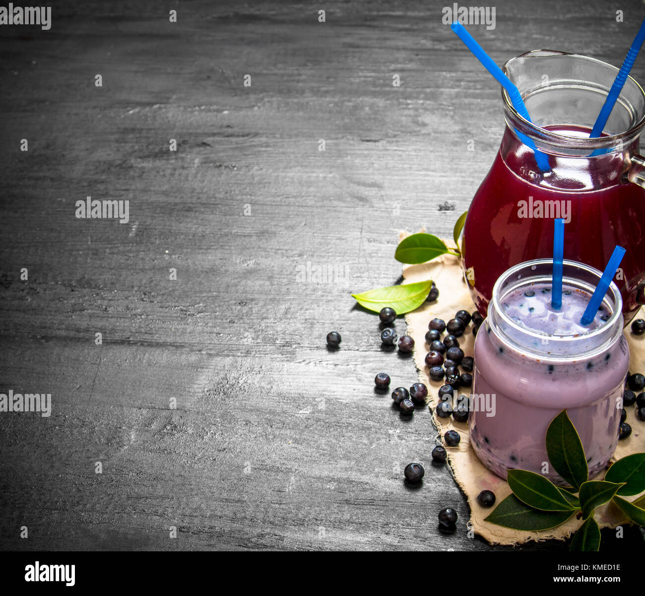 Blueberry smoothies and fresh juice on the old fabric. On a black wooden background. Stock Photo