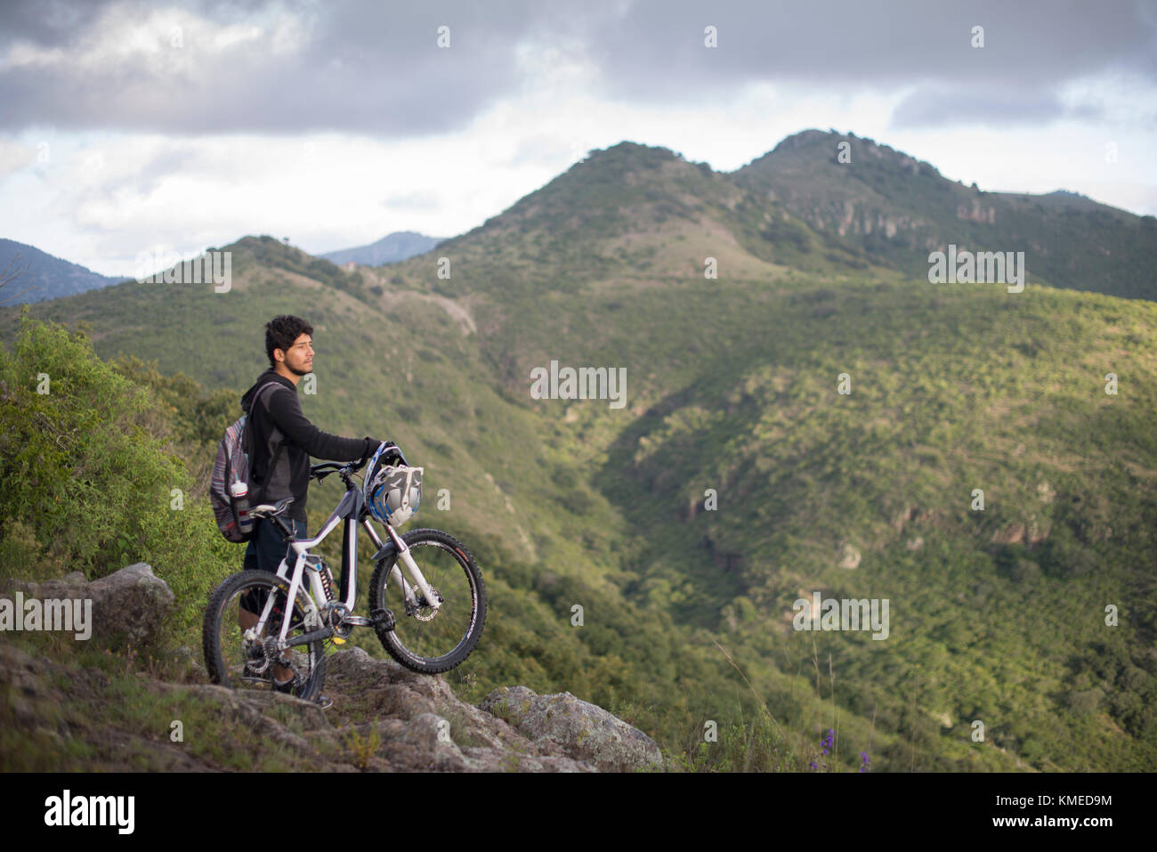 A mountain biker with his bike stears at the landscape during a trip at Joya La Barreta area in Queretaro, Mexico. Stock Photo