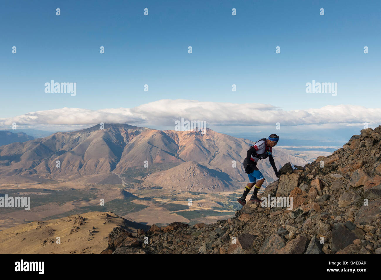 Man climbing rocky mountain against clouds and sky, Esquel, Chubut, Argentina Stock Photo