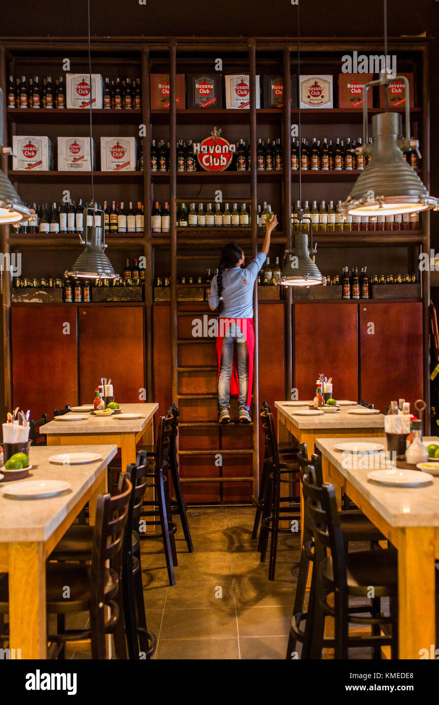 Woman pulling down bottle of rum at Central de Cevicheria, restaurant in Bogota, Colombia Stock Photo