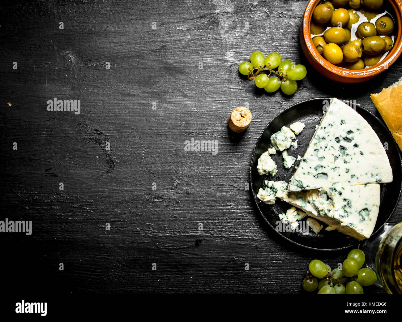 Blue cheese, olives and white grapes. On a black wooden background. Stock Photo