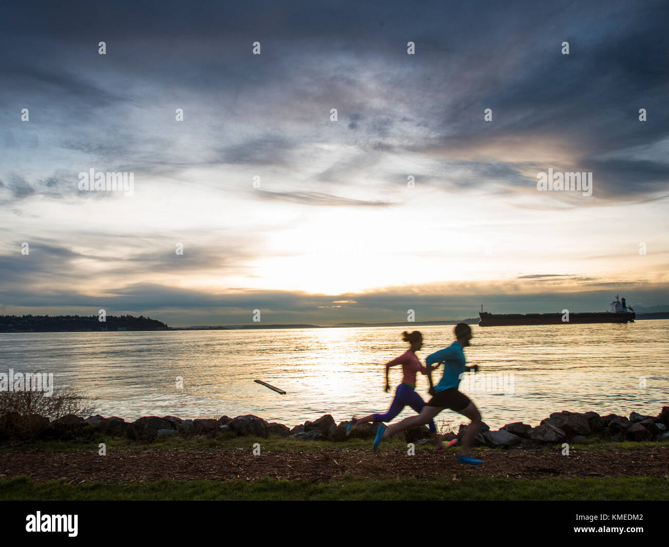 Two runners silhouetted against a colorful sky along the edge of the Puget Sound in Seattle, WA. Stock Photo