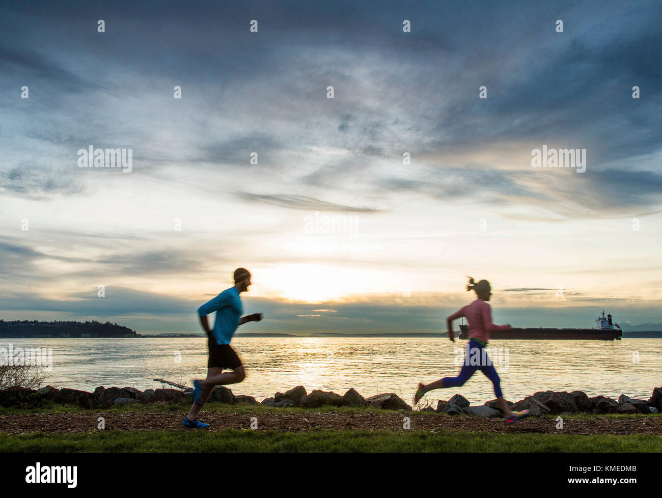 Two runners silhouetted against a colorful sky along the edge of the Puget Sound in Seattle, WA. Stock Photo
