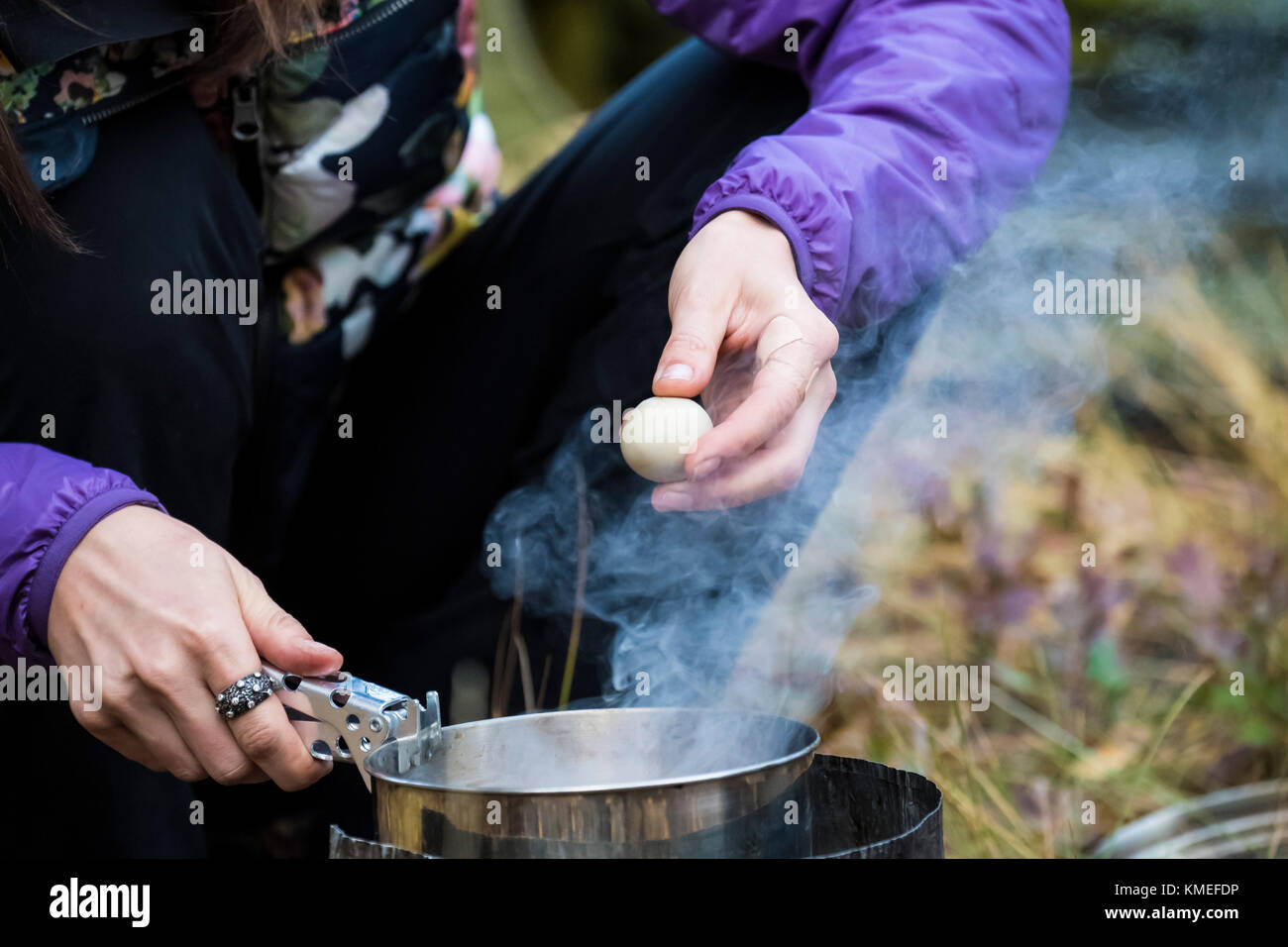 Close up of hands of female camper holding quail egg over steaming backpacking pot,Jackson,Wyoming,USA Stock Photo
