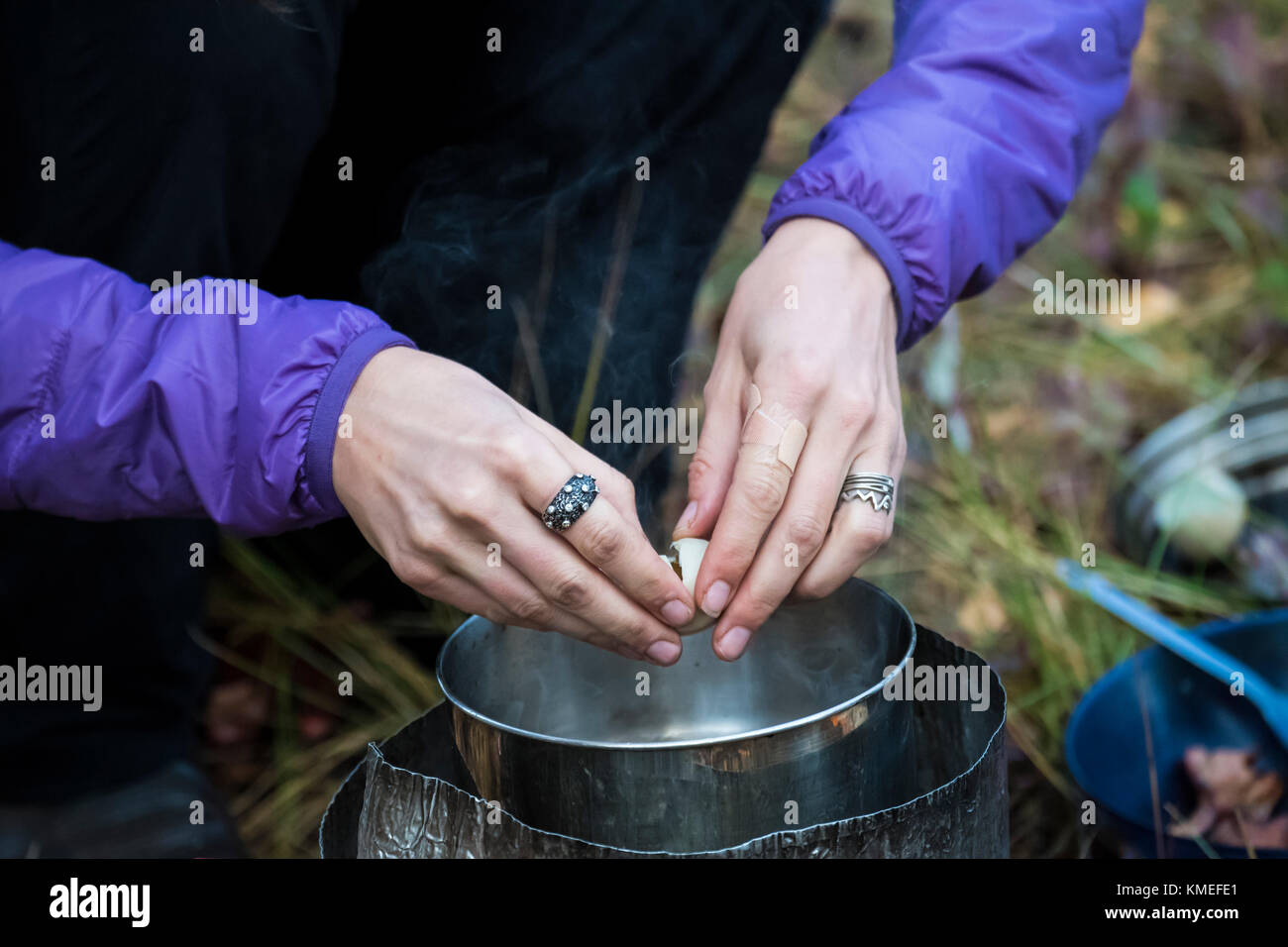 Close up of hands of female camper cracking quail egg into backpacking pot,Jackson,Wyoming,USA Stock Photo
