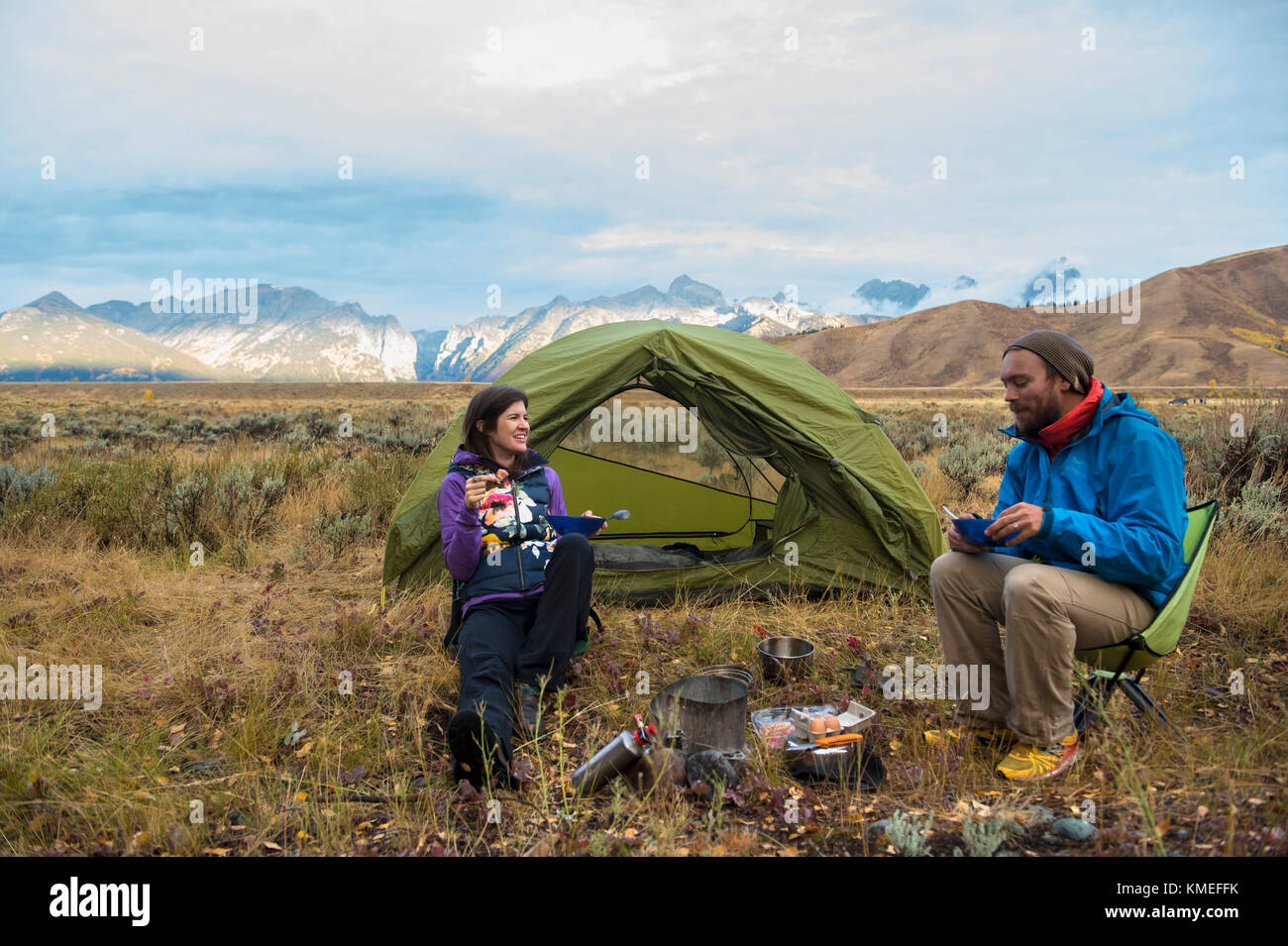Couple eating while camping in front of tent with mountains of Teton Range in background,Jackson,Wyoming,USA Stock Photo