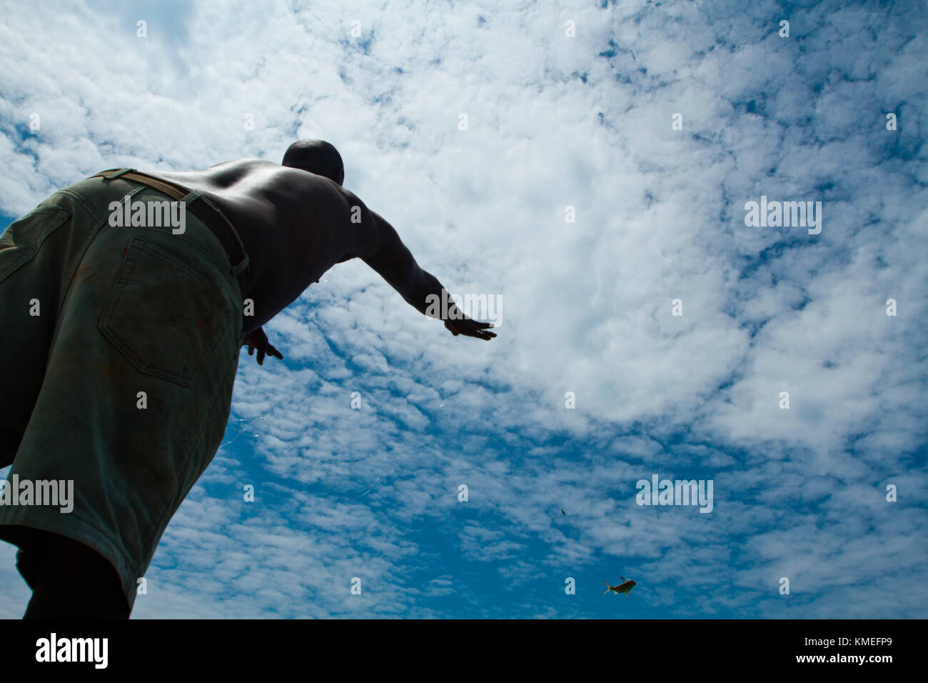 View from below of shirtless man casting fishing line, Isla Marisol, Belize Stock Photo
