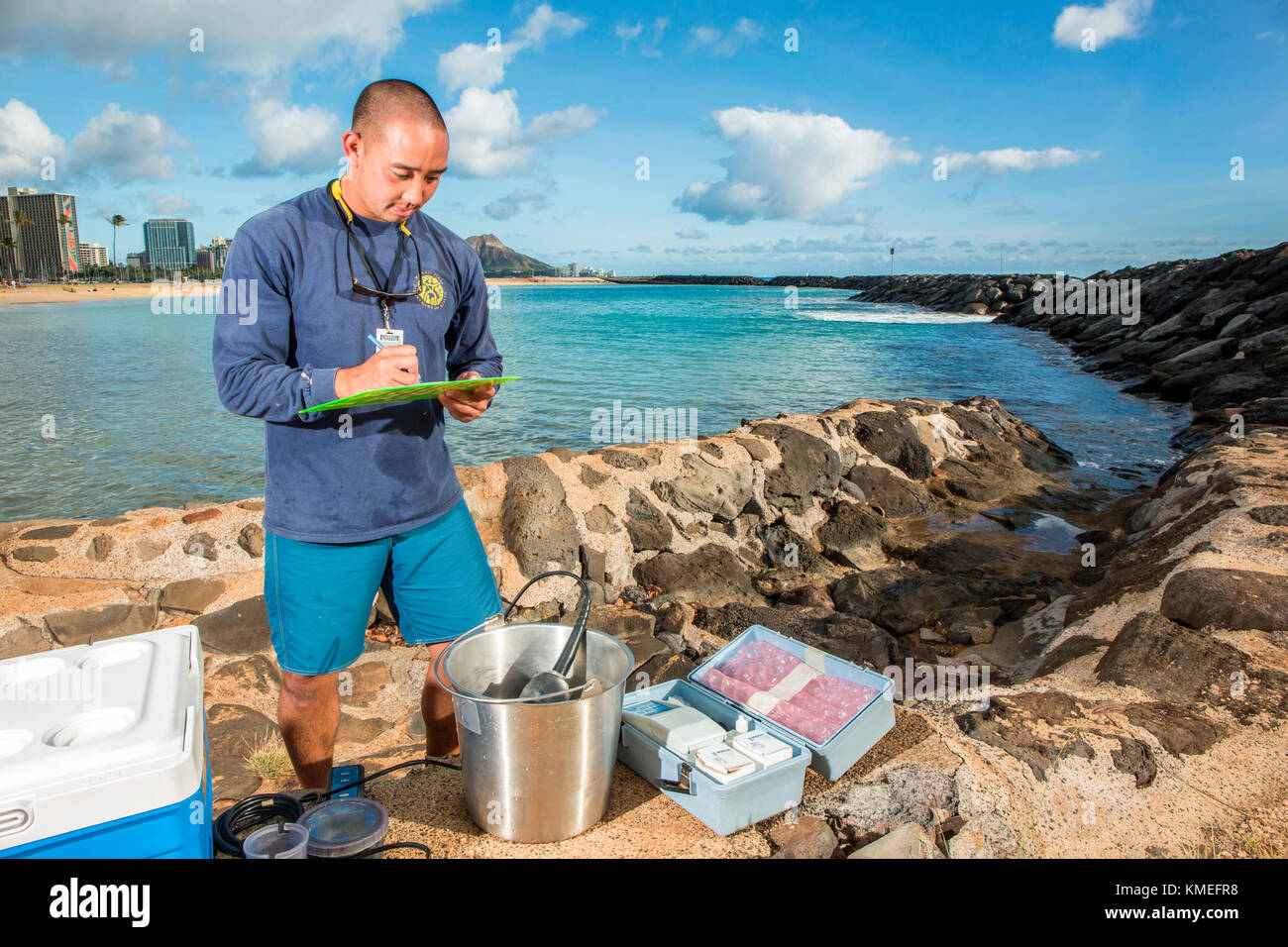 Wataru Kumagai of the State of Hawaii Department of Health Clean Water Branch,demonstrates water sampling of Hawaiian beaches at Ala Moana Beach in Honolulu using instruments such as a turbidity meter.For the full scope of readings,lab work has be done offsite. Stock Photo