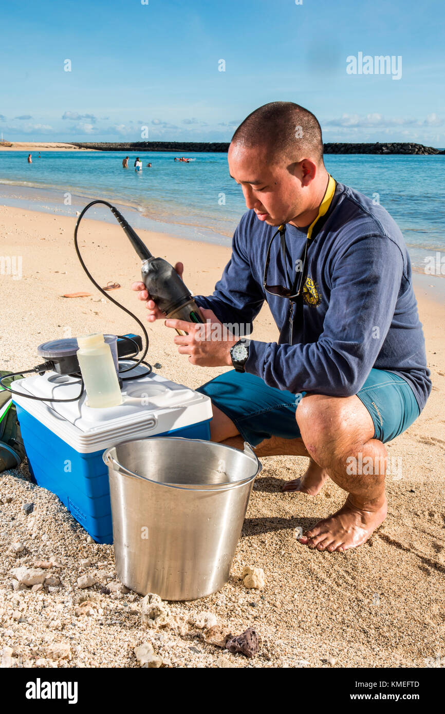 Wataru Kumagai of the State of Hawaii Department of Health Clean Water Branch,demonstrates water sampling of Hawaiian beaches at Ala Moana Beach in Honolulu using instruments such as a turbidity meter.For the full scope of readings,lab work has be done offsite. Stock Photo