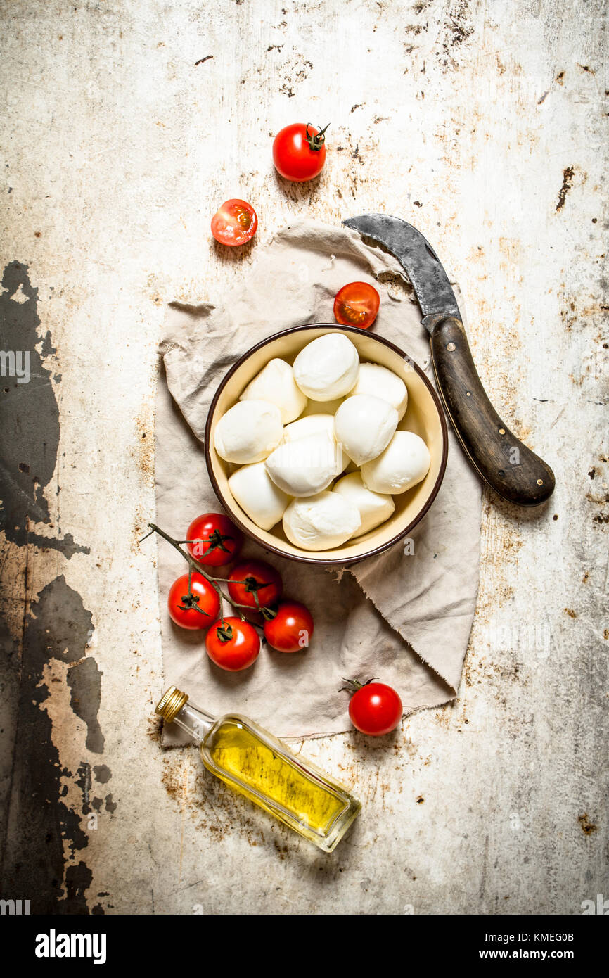 Mozzarella cheese, tomatoes, olive oil and an old knife. On rustic