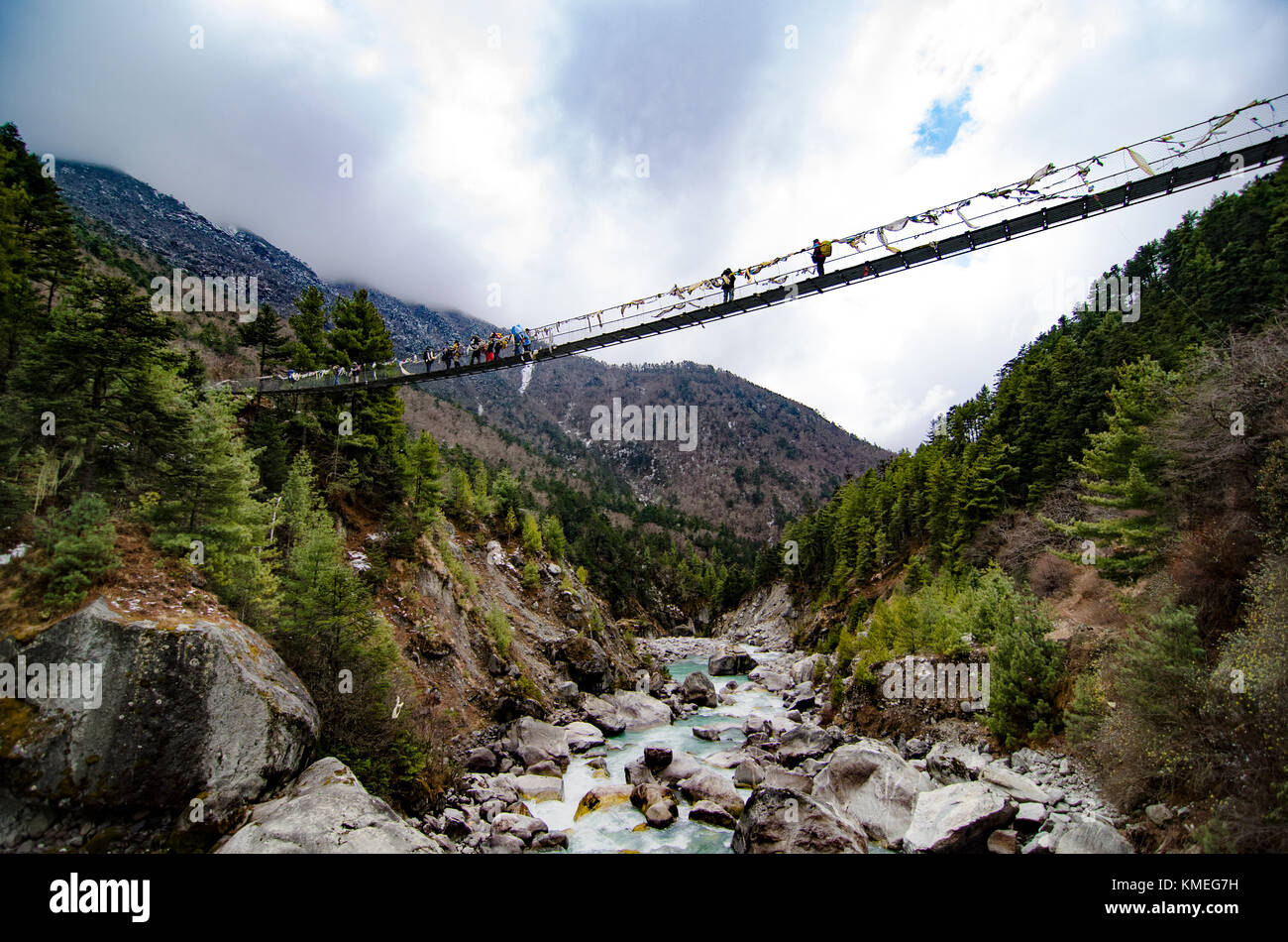 Trekkers crossing suspension bridge hanging over rocks and stream, Solukhumbu, Nepal Stock Photo
