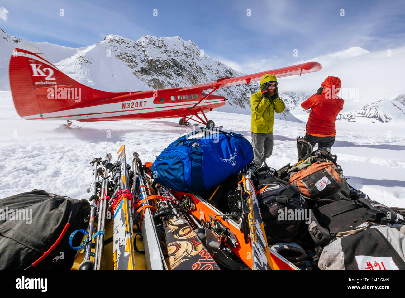 Two mountain climbers standing near baggage and protecting ears from noise of airplane taking off, Denali National Park, Alaska, USA Stock Photo