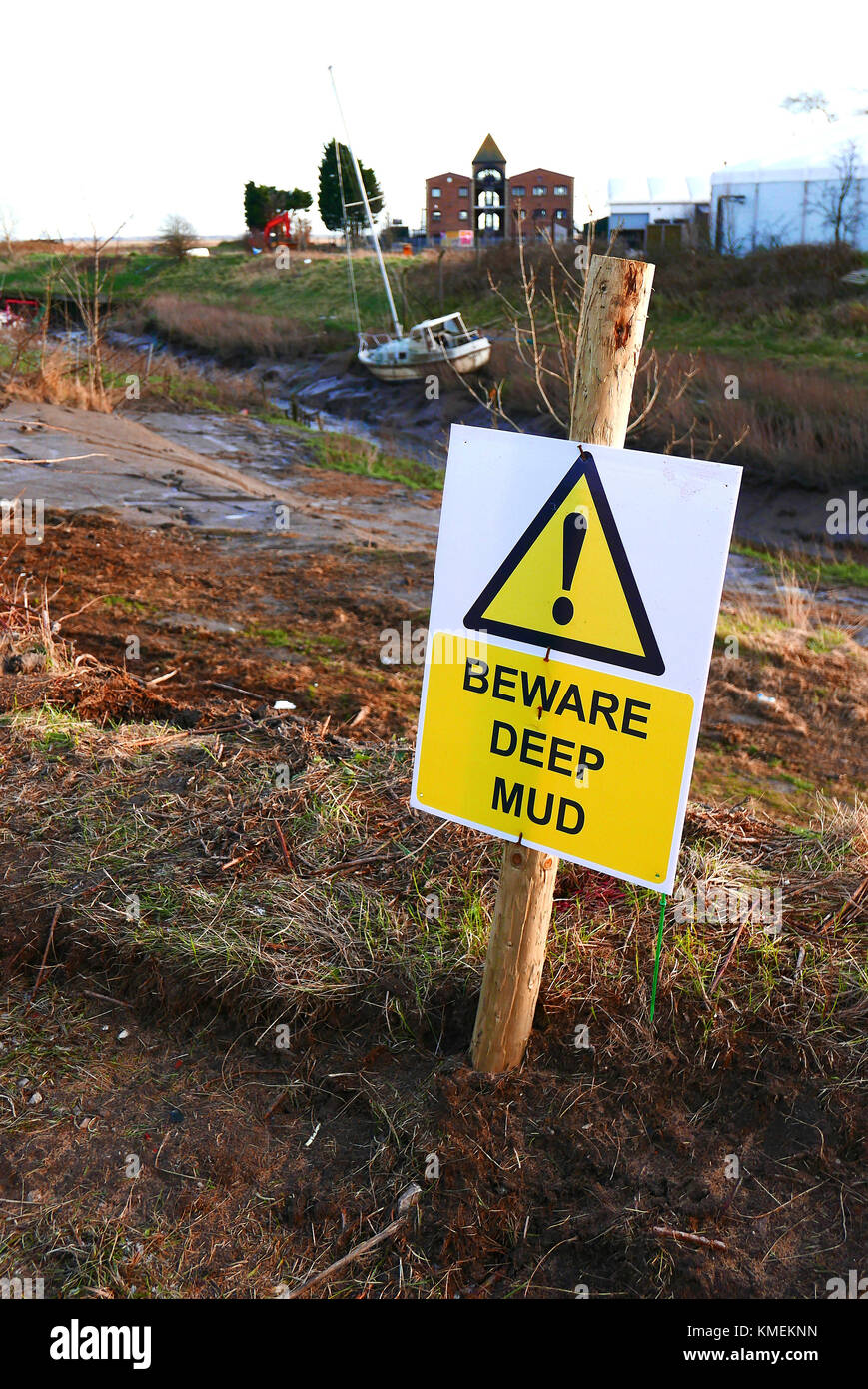 Beware deep mud sign on banks of small creek with grounded boat in background Stock Photo
