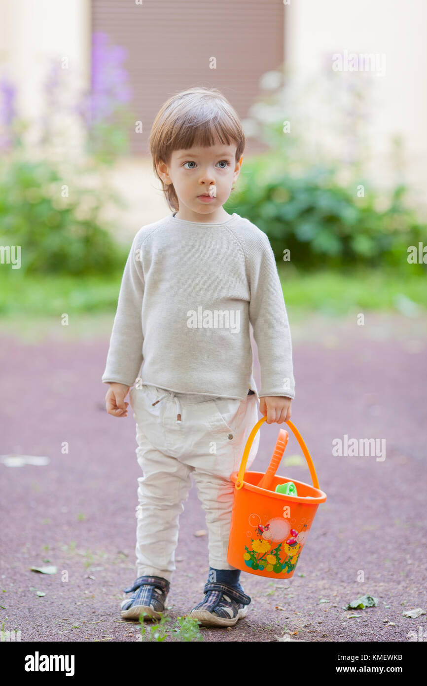 Little Beautiful Boy With Long Hair And Blue Eyes Holding A Bucket