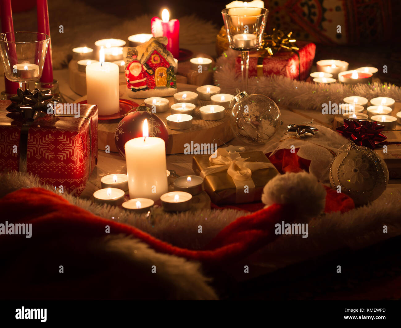 Christmas still life with candles of different size and shape, decorative round wood, souvenir Santa Claus clay house, gift boxes, christmas tree toy. Stock Photo