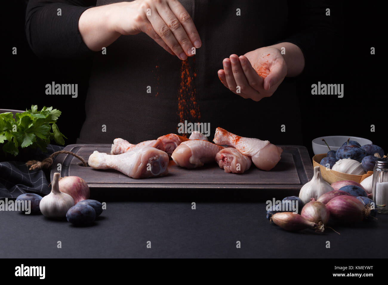 A Female Chef Sprinkles Fresh Raw Chicken Drumsticks On A Dark Stock