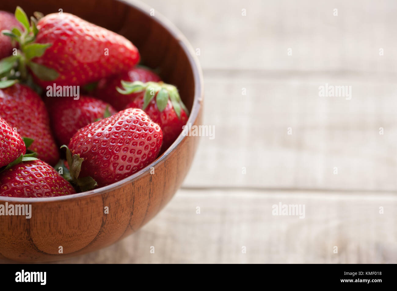 Fresh strawberries in a wooden bowl on a wooden table. Top view with ...