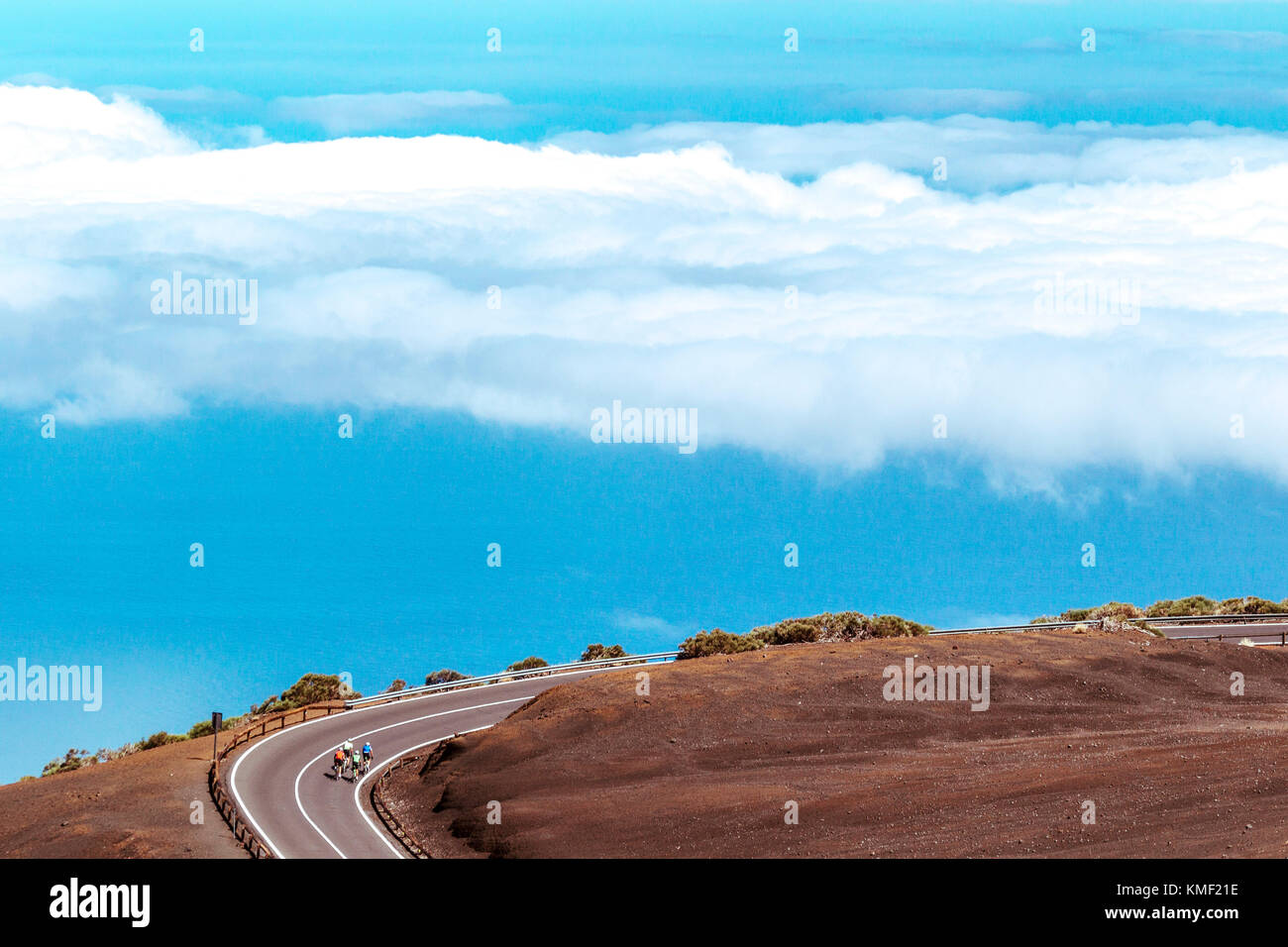 Cyclists pedaling on winding mountain road above clouds,Teide National Park,Tenerife,Canary Islands,Spain Stock Photo