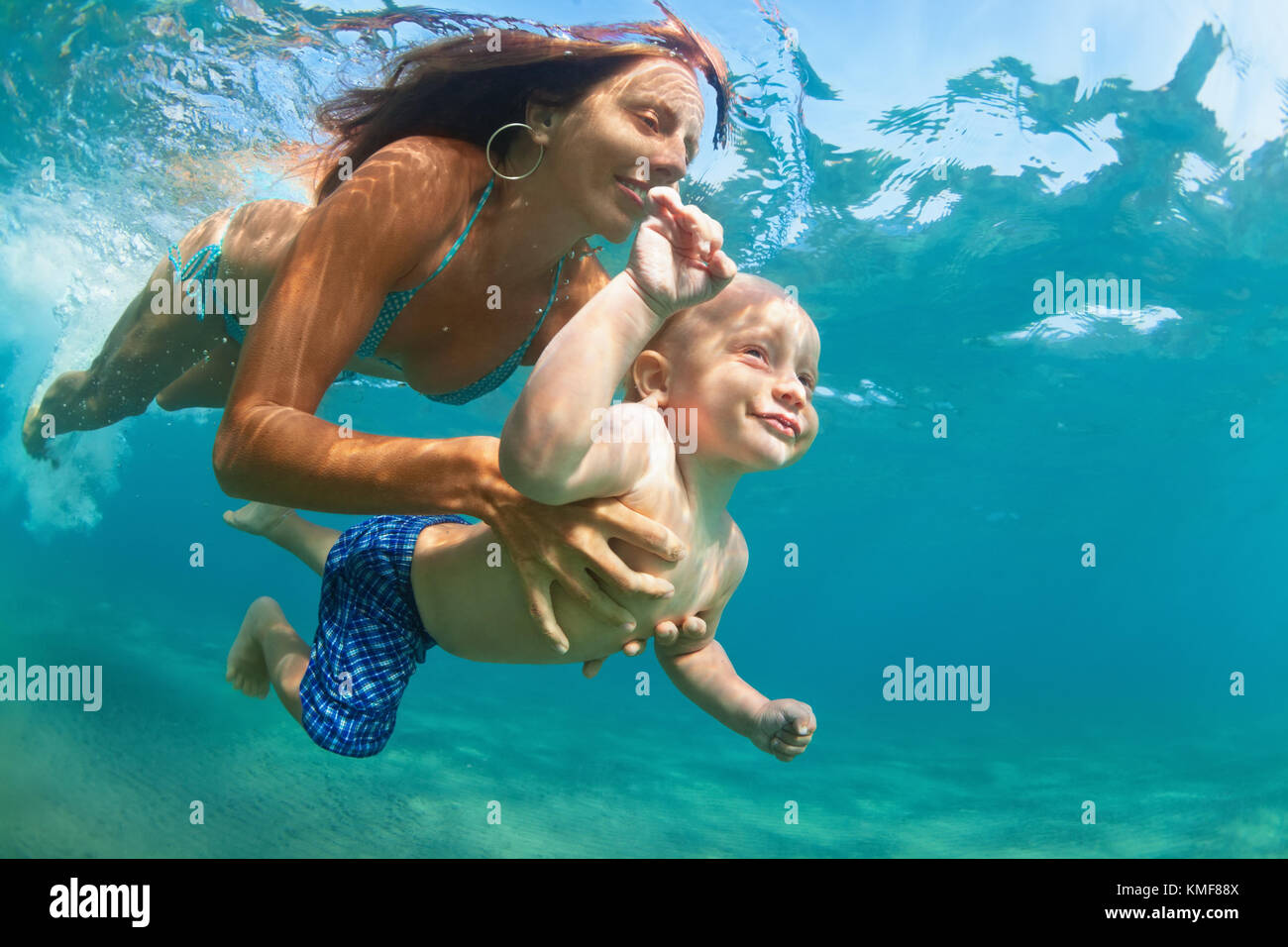 Happy family - mother with baby son dive underwater with fun in sea pool. Healthy lifestyle, active parent, people water sport outdoor adventure. Stock Photo