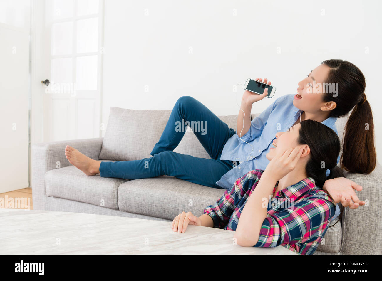 Cheerful Beauty Girl Lying Down On Sofa Couch And Using Mobile