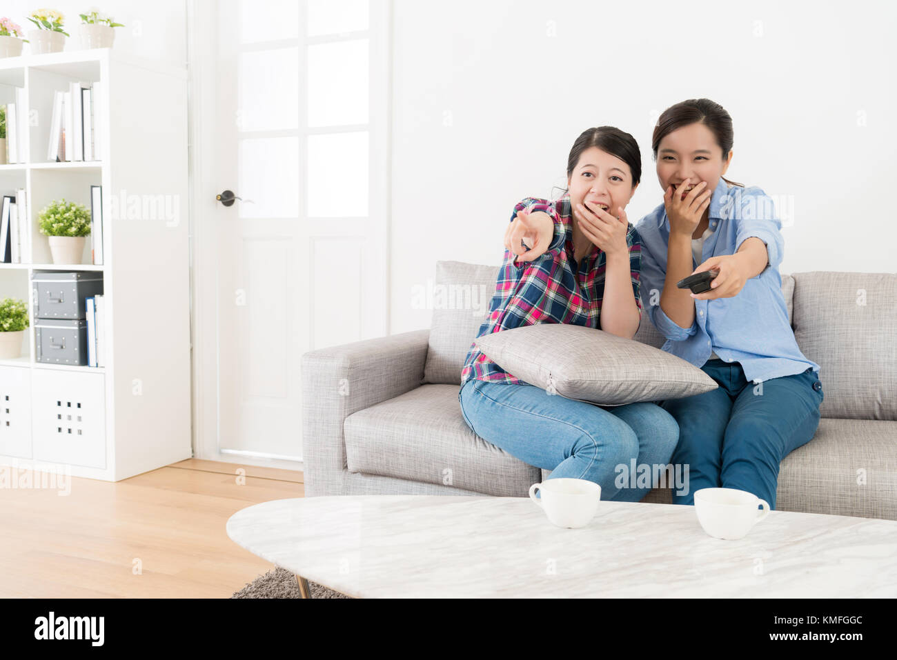 young happy women friends sitting on living room sofa at home watching tv  together and looking at comedy program laughing Stock Photo - Alamy