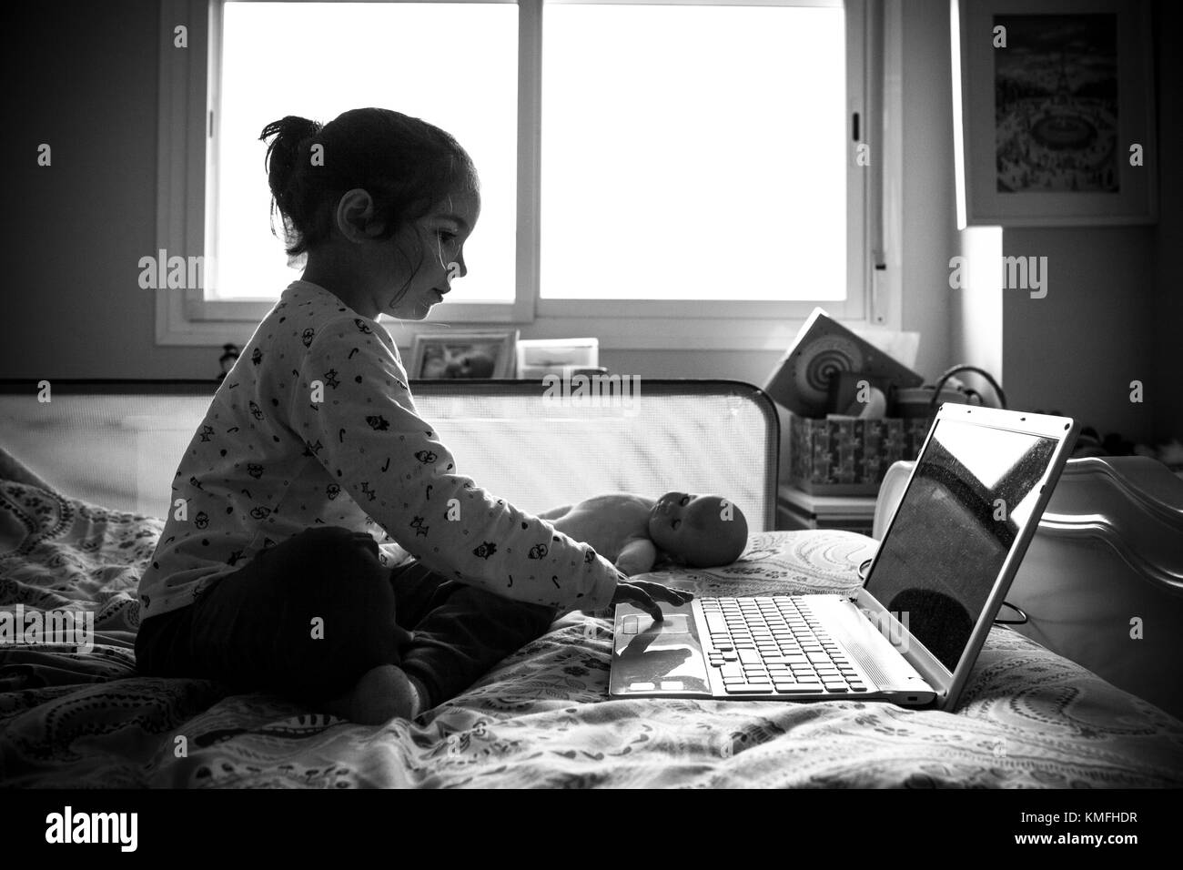 Little girl sitting in bed and playing online games in his bedroom. Black and white shot Stock Photo