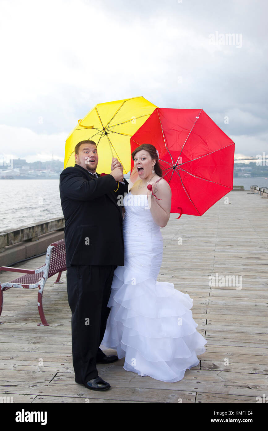newlyweds with yellow and red umbrellas get blown away by a storm Stock Photo