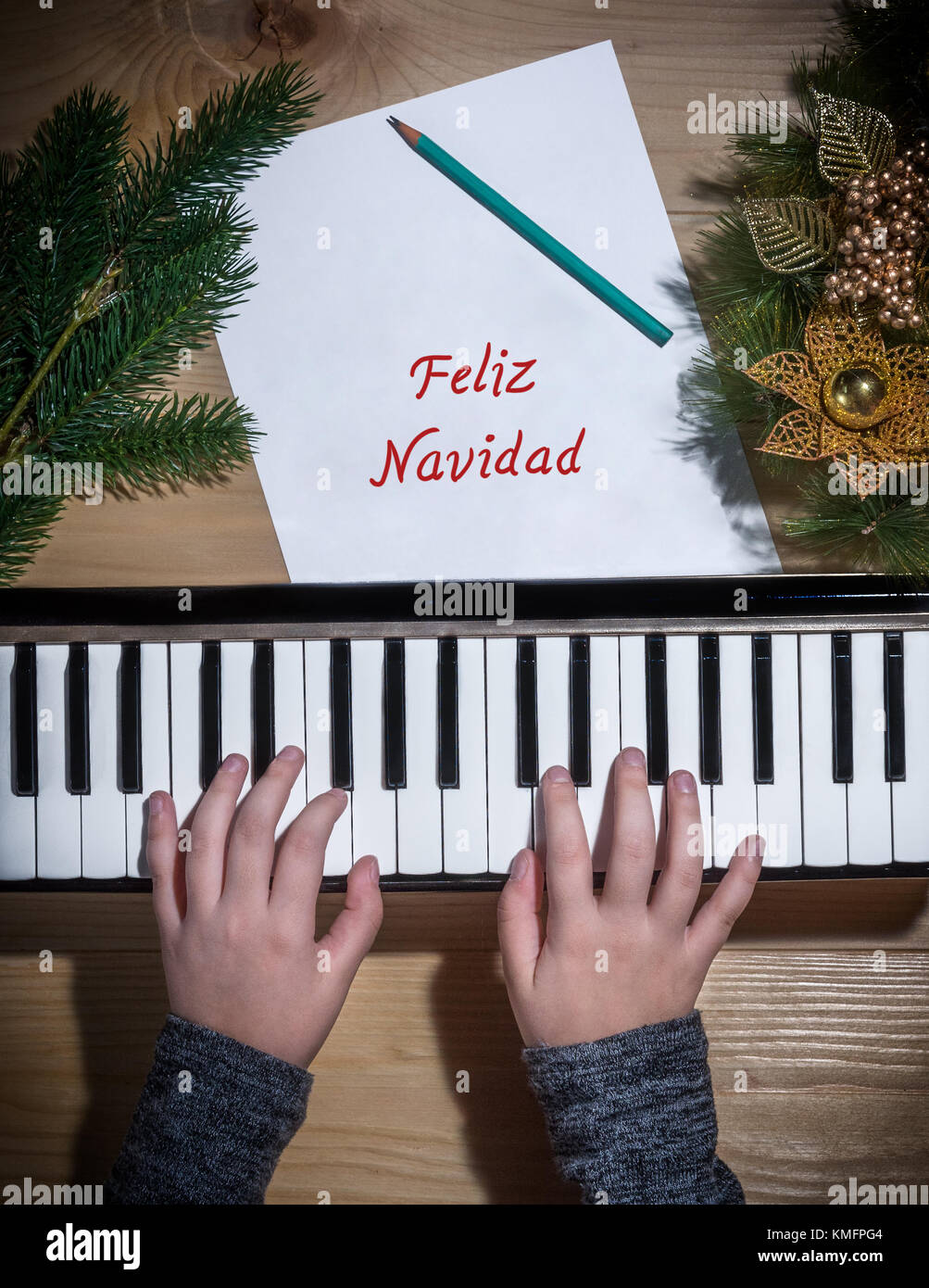 Feliz Navidad - Young hands of a girl playing on a keyboard with Christmas decorations on a wooden table Stock Photo