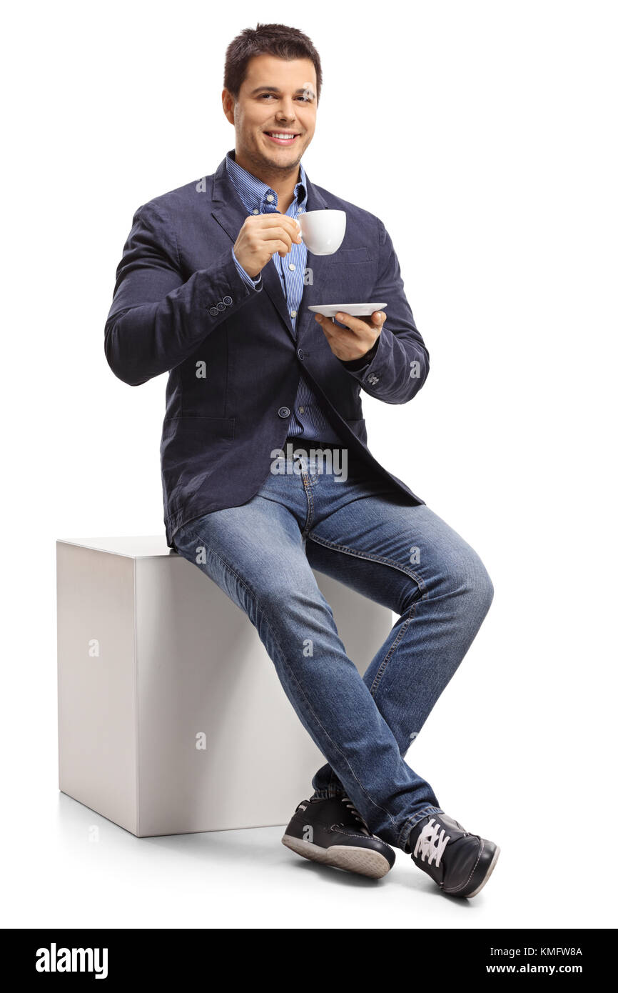 Elegant guy sitting on a cube and holding a cup isolated on white background Stock Photo