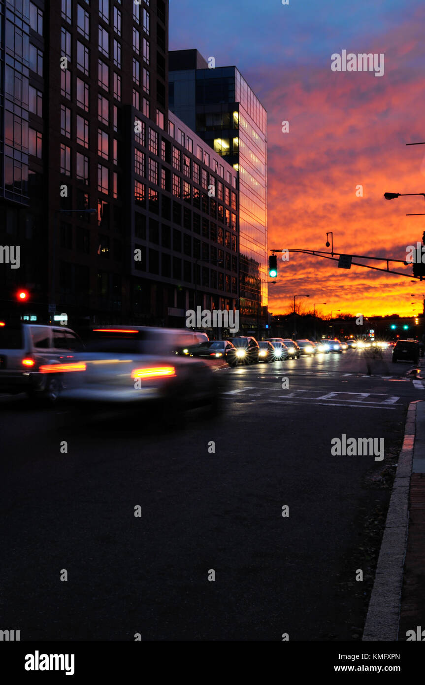 End of work day background. Night traffic and sunset sky at rush hour. Cars leaving city, scattered lights on office building, colorful and dark. Stock Photo