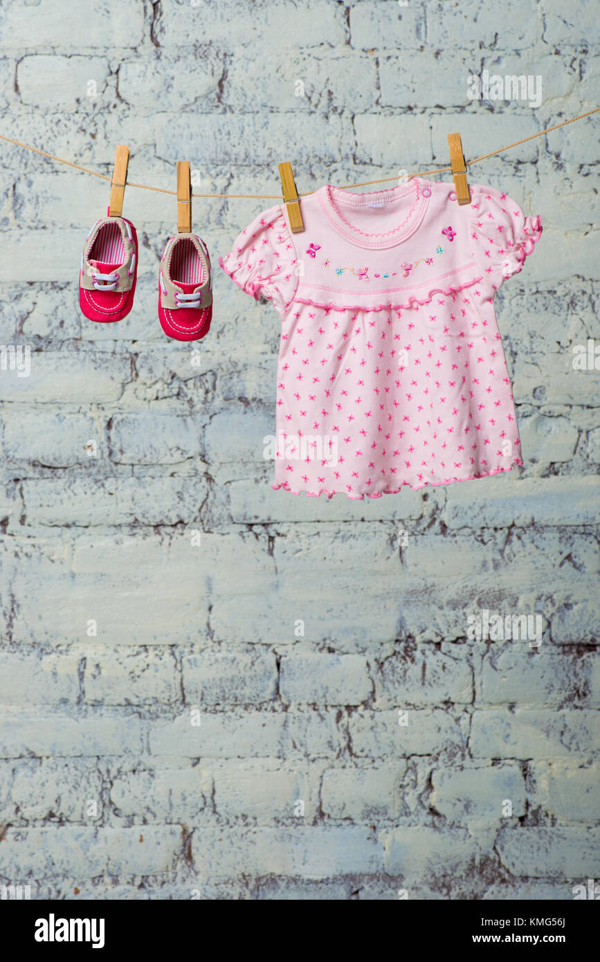 Baby pink dress and red shoes for the girl, dry on a rope against a ...