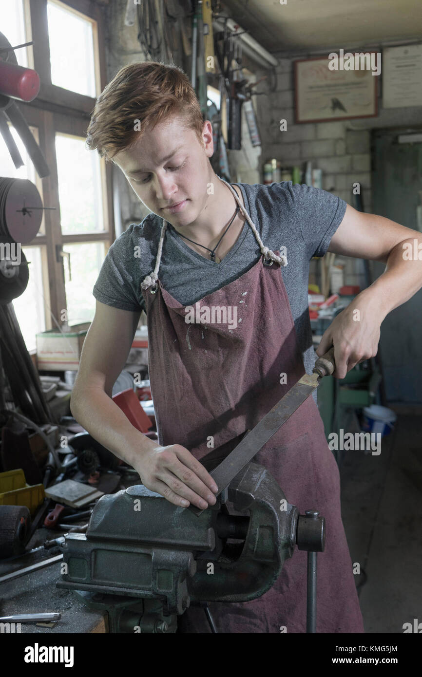 Blacksmith apprentice rasping iron fixed in plain vise Stock Photo