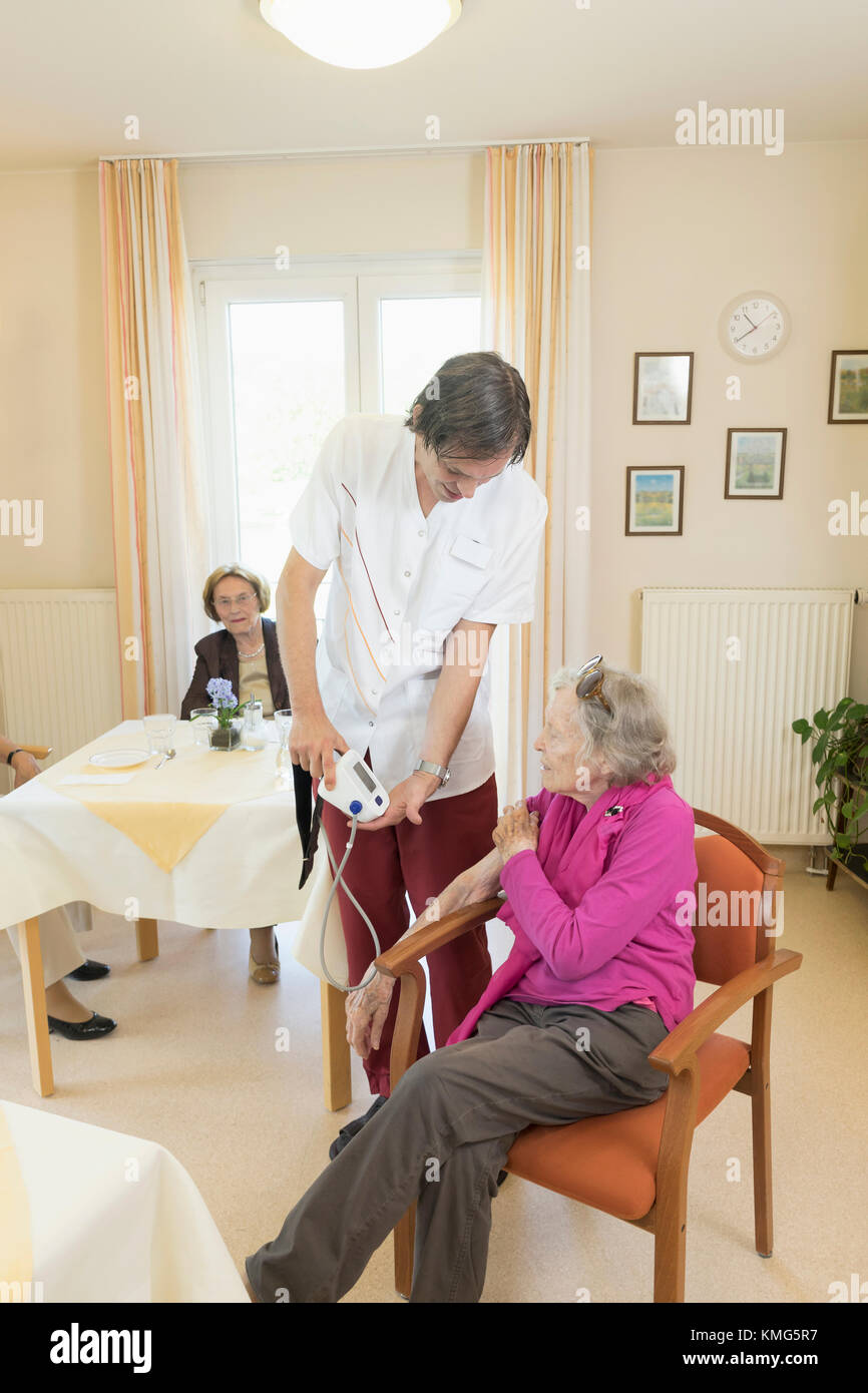 Caretaker checking blood pressure of senior woman in rest home Stock Photo