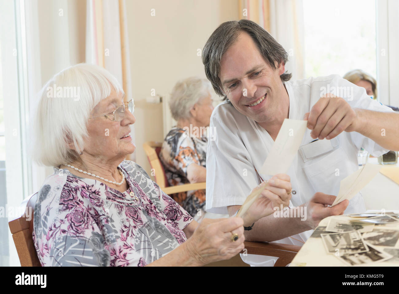 Caretaker watching photos with senior women at rest home Stock Photo