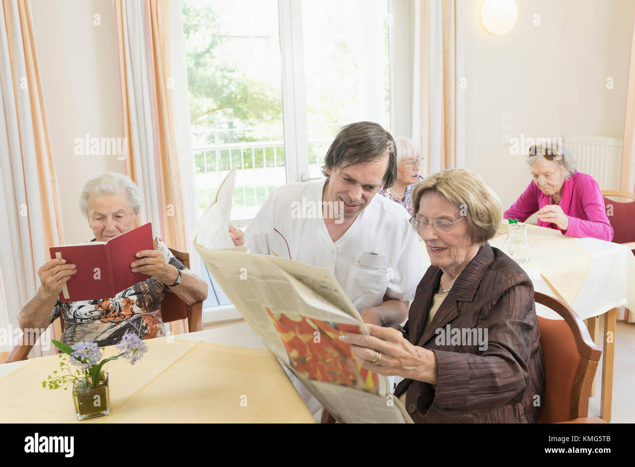 Caretaker reading newspaper with senior woman in rest home Stock Photo