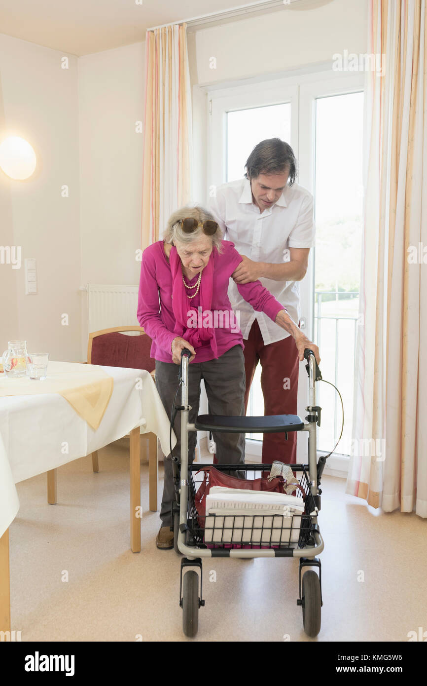 Caretaker helping senior woman using wheeled walker Stock Photo