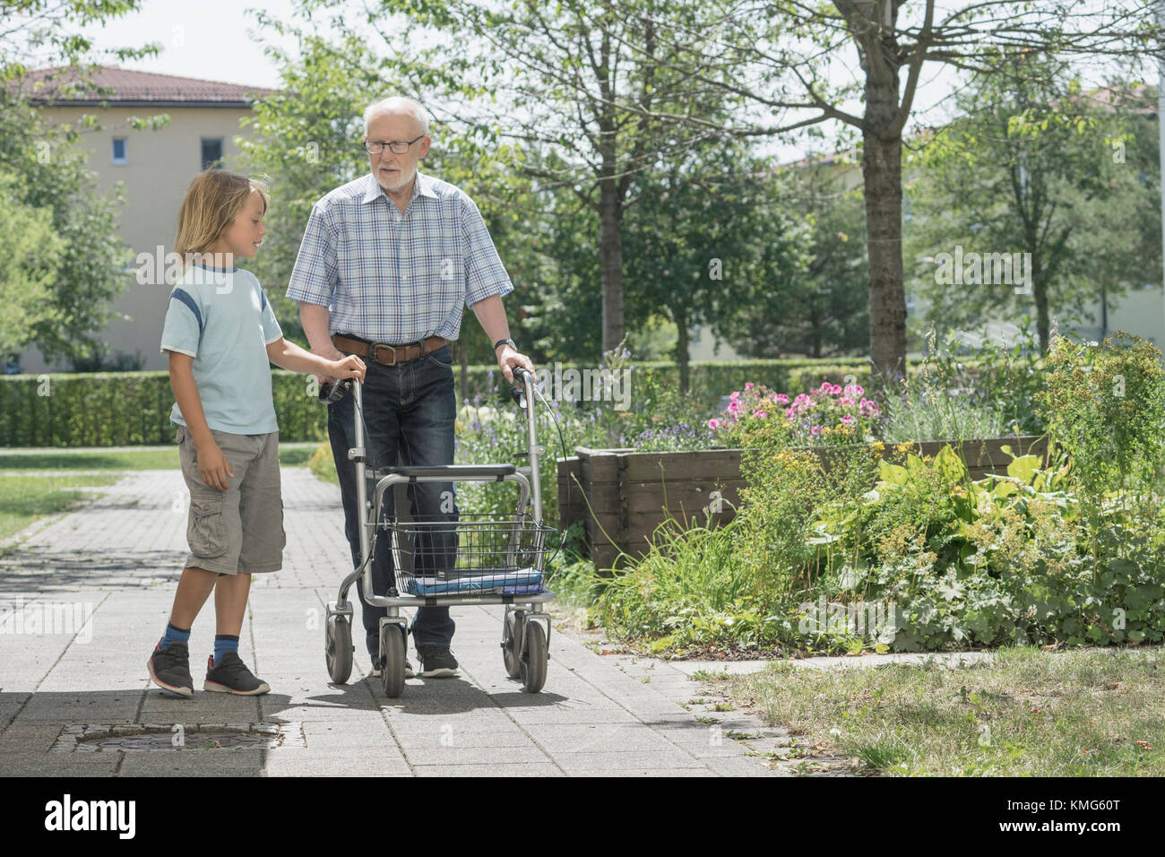 Boy helping grandfather with mobility walker at rest home park Stock Photo