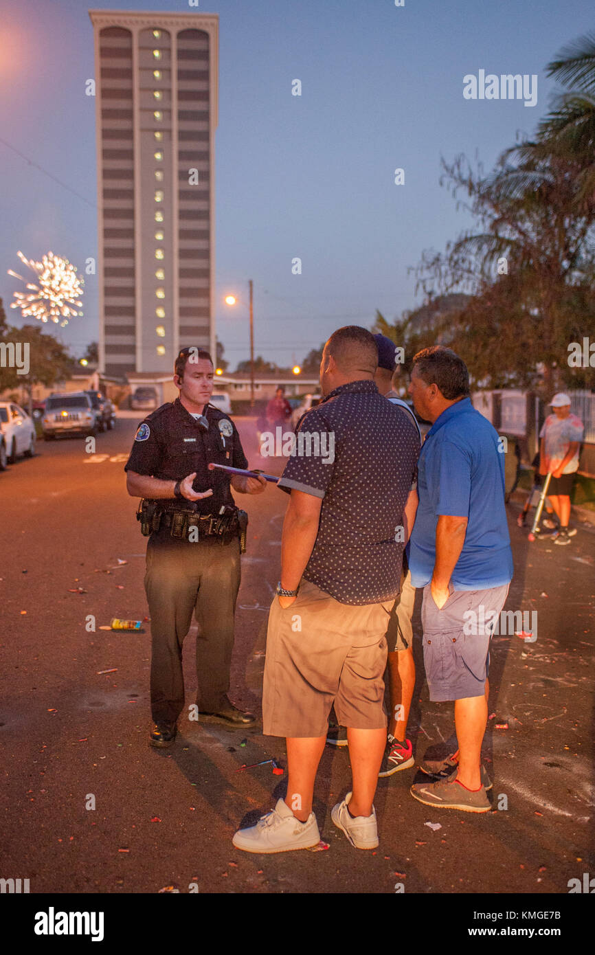 A Costa Mesa, CA, policeman writes a a citation after apprehending a Hispanic local man for use of illegal fireworks on July 4th. Note fireworks exploding in background. Stock Photo
