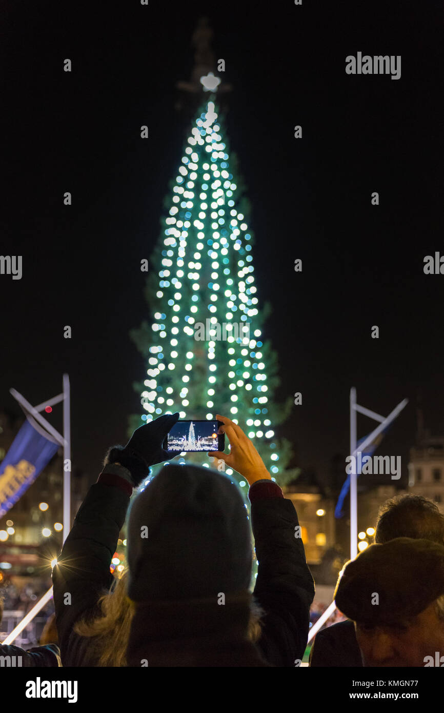 Trafalgar Square, London, 7th Dec 2017. A woman takes snaps of the illumunated tree. The annual Trafalgar Square Christmas Tree lighting ceremony takes place in the square, with tourists and Londoners watching the official switch on, as well as carols and choral singing in festive atmosphere. The Trafalgar Square Christmas tree is hand picked and donated to the people of Britain by the city of Oslo, Norway each year since 1947, and 2017 is its 70th anniversary. Stock Photo